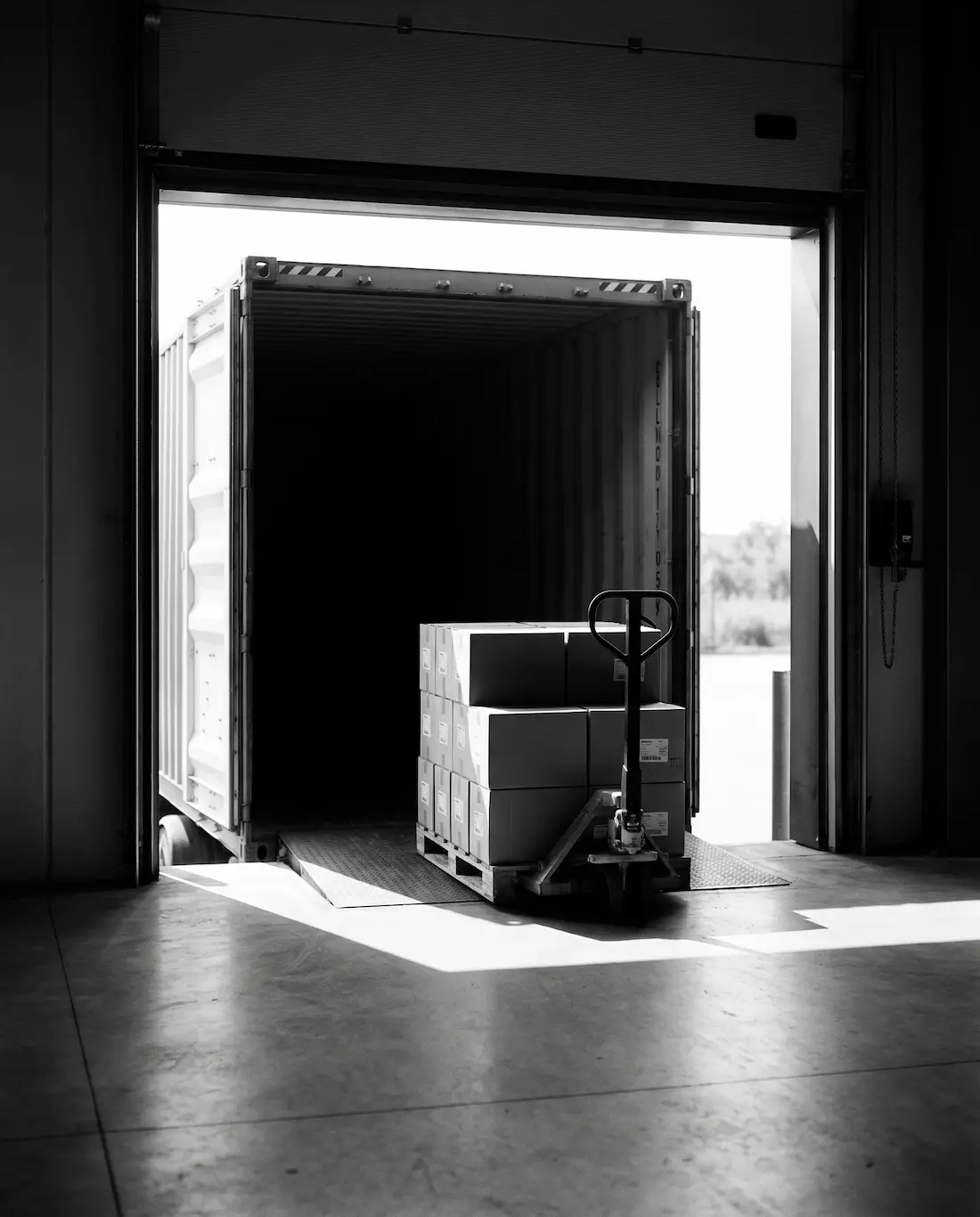 A container at a warehouse dock door being unloaded with a pallet jack
